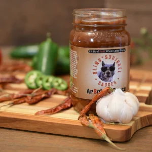 Blind Squirrel Arbol sauce on a wooden board, surrounded by peppers & garlic.